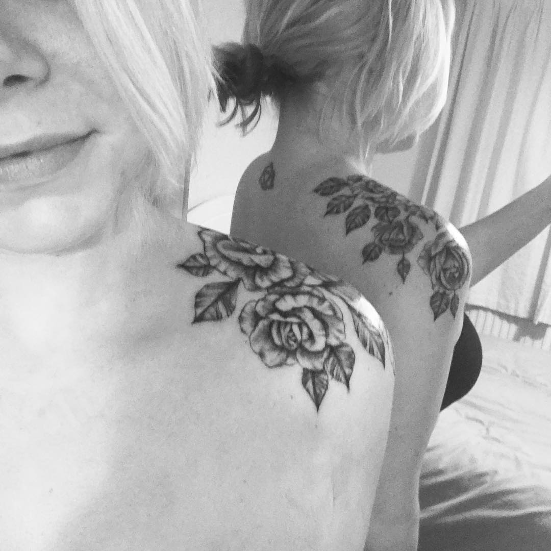 Woman views her rose shoulder tattoo in mirror